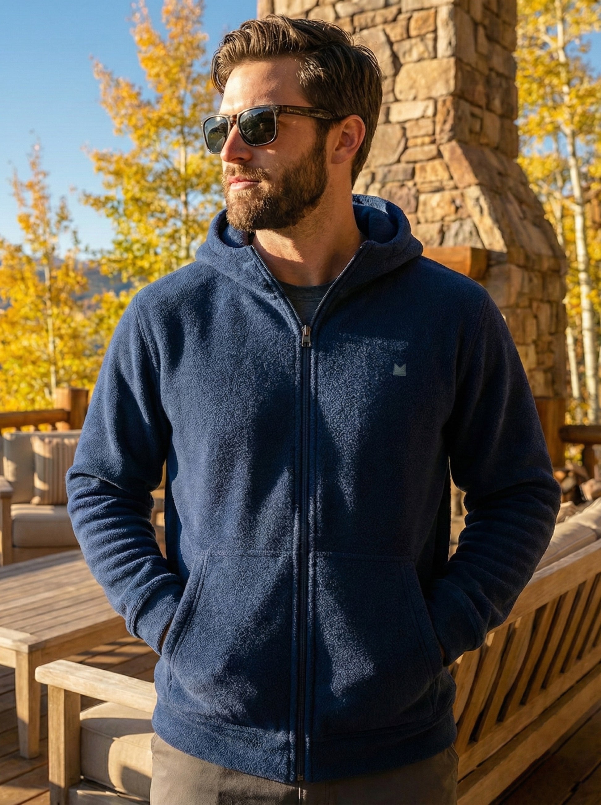 Man wearing a navy blue fleece jacket with a logo, standing outdoors in autumn.